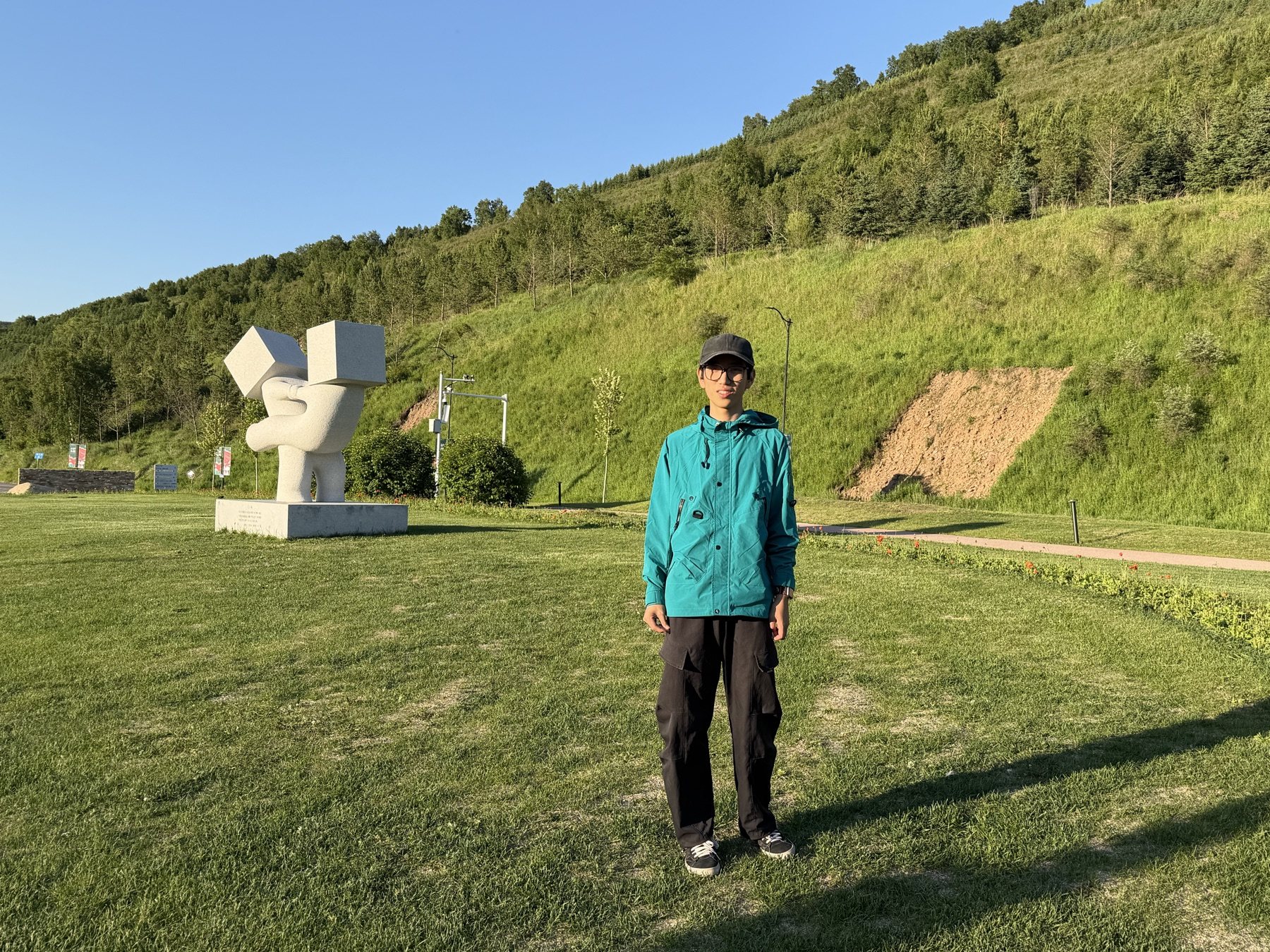齐恩贺站在草地和山坡前